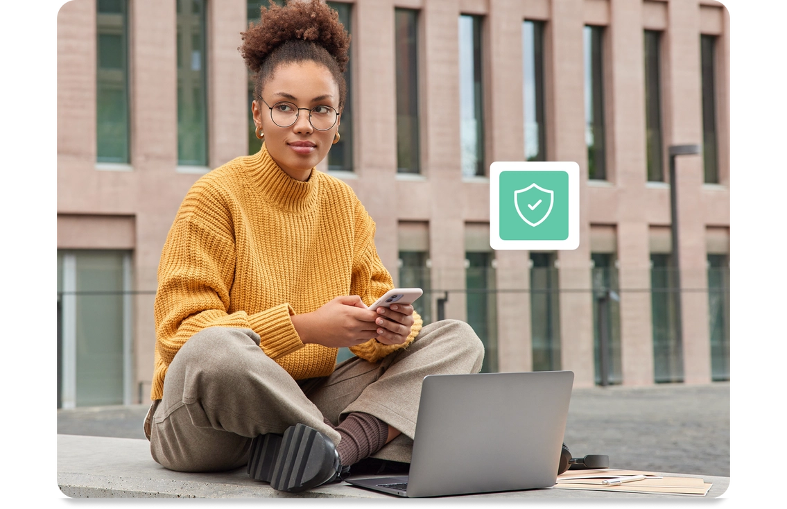 Jauna sieviete ar brillēm un dzeltenu džemperi sēž ārā sakrustotām kājām ar klēpjdatoru un viedtālruni. Attēla pārklājumā redzams teksts “Integrētie B2B risinājumi” ar zaļas vairoga ikonu.