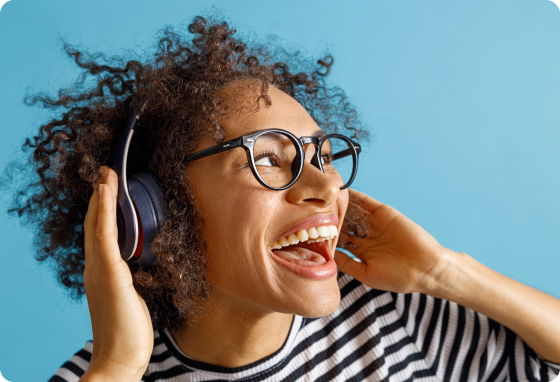 Attēls ar tuvplānu cilvēkam svītrainā kreklā, ar brillēm un austiņām, kurš smaidot klausās audio.