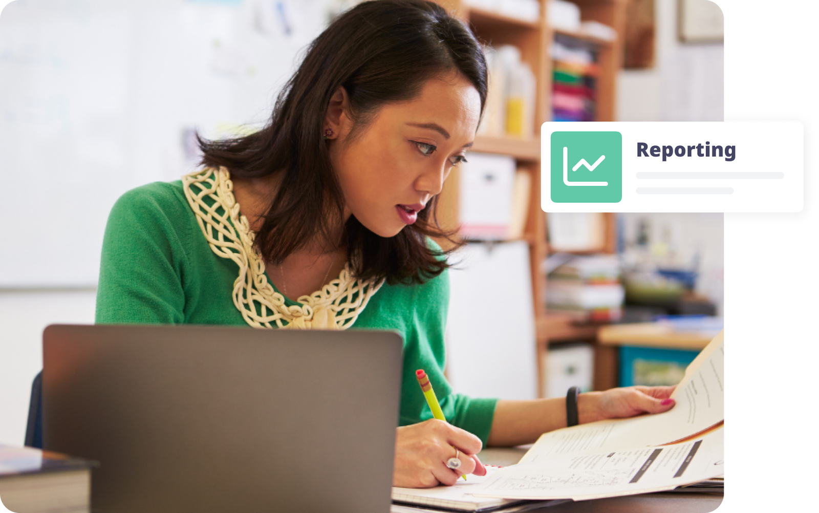 Woman analyzing reports at a desk with a laptop, focused on her work and taking notes.