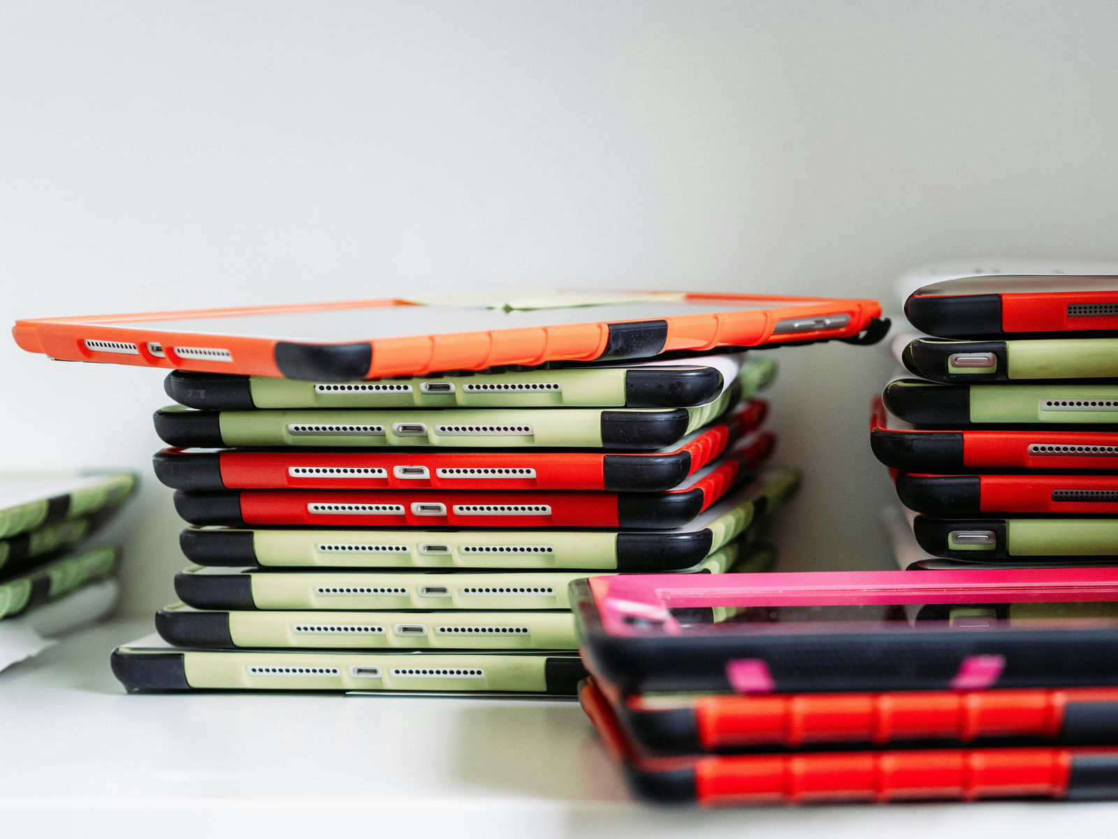 Stacked tablets with colorful cases in red, green, and black on a shelf.
