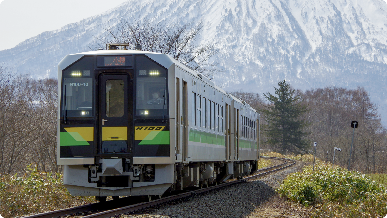 Train traveling along a scenic track with snow-capped mountains in the background.