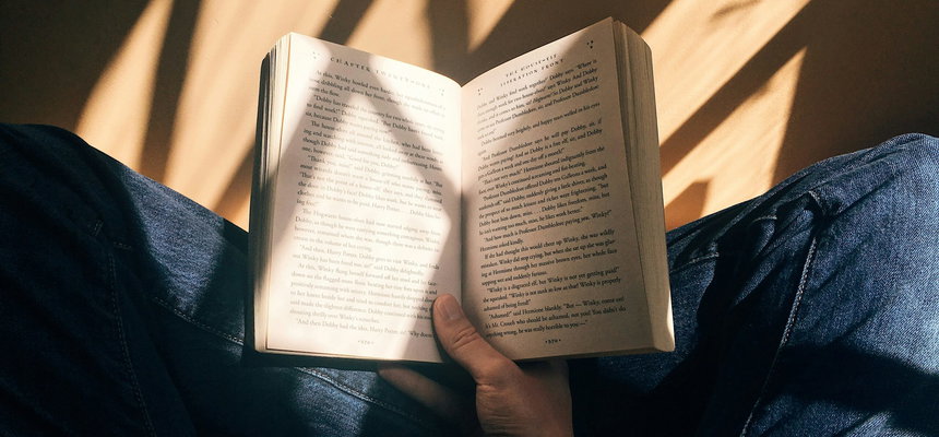 A person sitting on a chair, engrossed in an open book, captivated by the words on its pages.