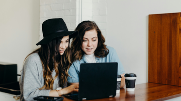 Two women sitting in front of a table where a computer is placed