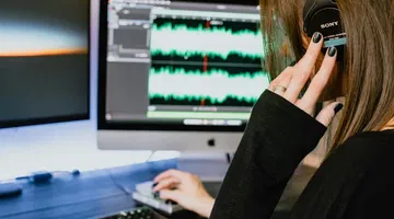 Una donna con le cuffie usa un laptop dove vediamo una registrazione vocale.