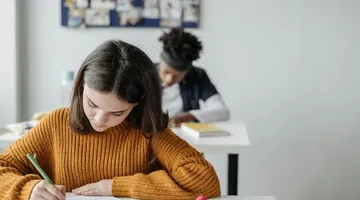 Student in knitted sweater writing in her notebook - the ADA Title II web accessibility rule in public education