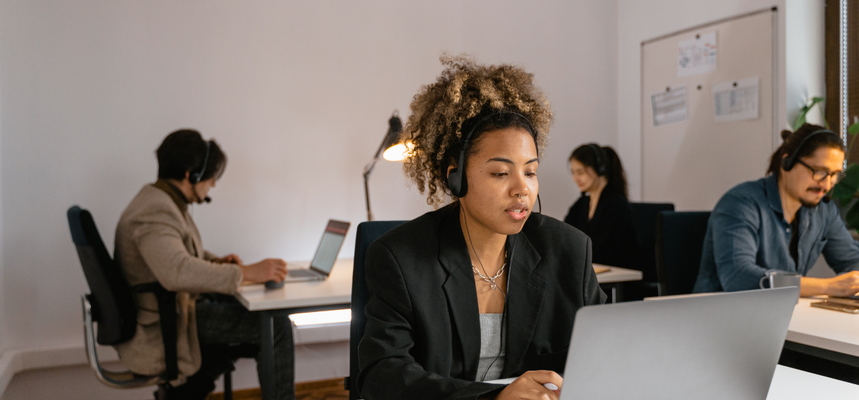 A woman in front of a PC with a headset.
