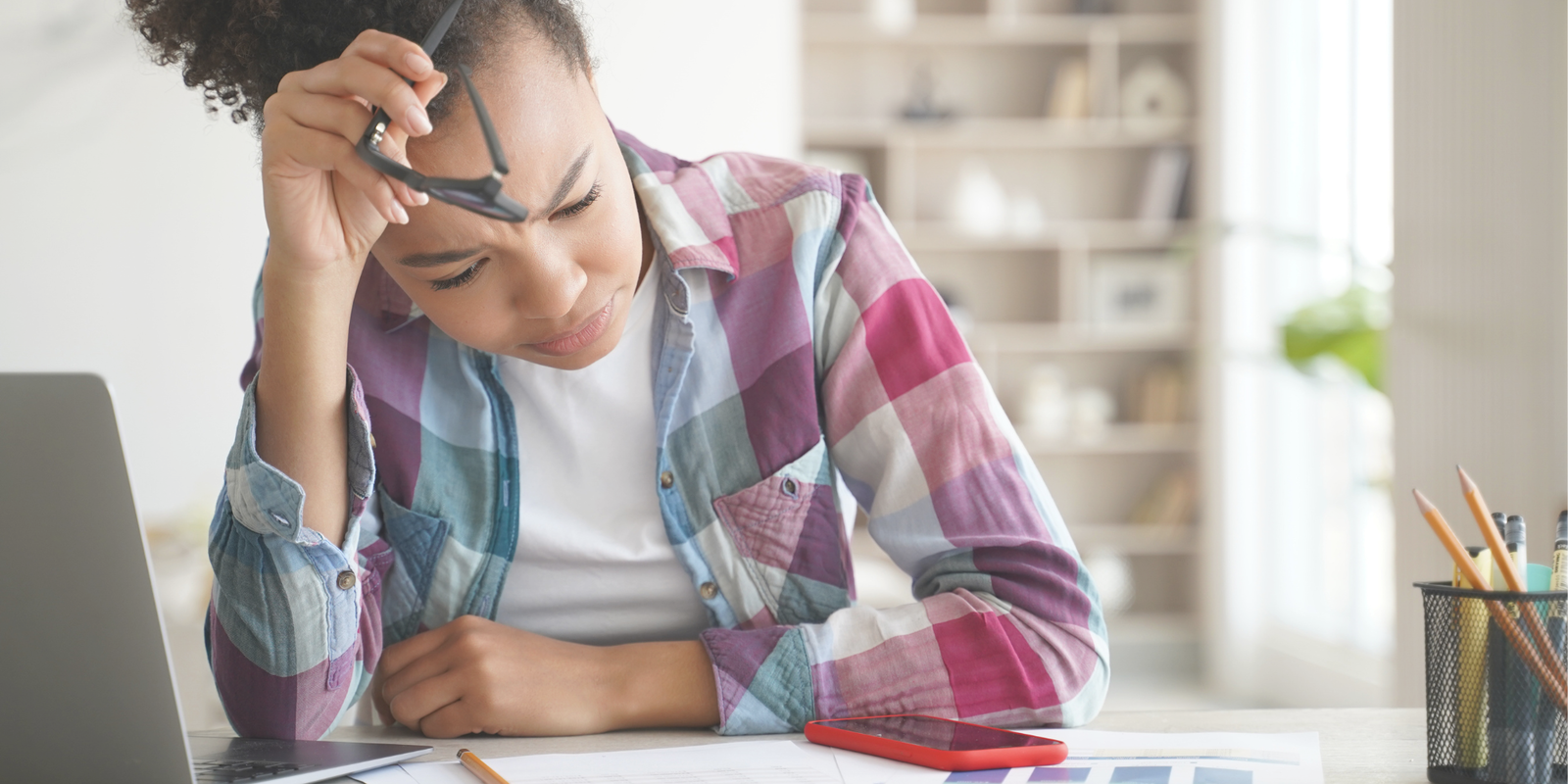 A girl in front of her computer looks at her smartphone.