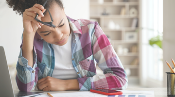A girl in front of her computer looks at her smartphone.