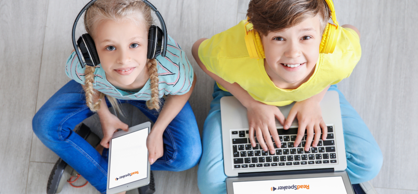 Two children are using computers while smiling.