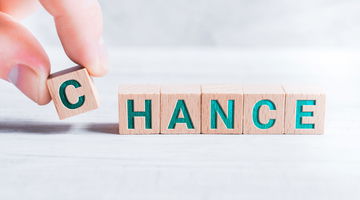 The Word Chance Formed By Wooden Blocks And Arranged By Male Fingers On White Table