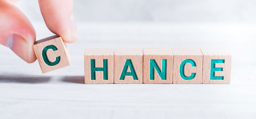 The Word Chance Formed By Wooden Blocks And Arranged By Male Fingers On White Table