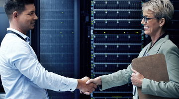 Two technicians shaking hands while working together in a server room.