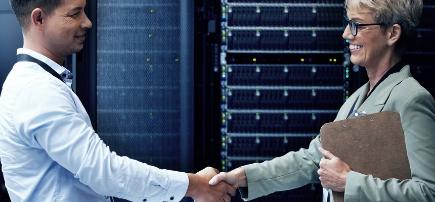 Two technicians shaking hands while working together in a server room.