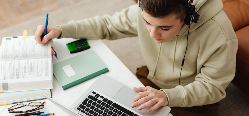 Étudiant assis à un bureau utilisant un ordinateur portable et un casque pour un apprentissage accessible..
