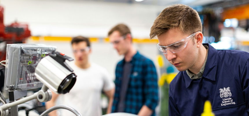 Engineering students, wearing goggles, standing by machinery, representing accessibility in vocational training.