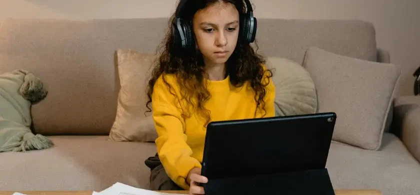 Une étudiante portant un casque audio regarde une tablette posée sur une table basse.