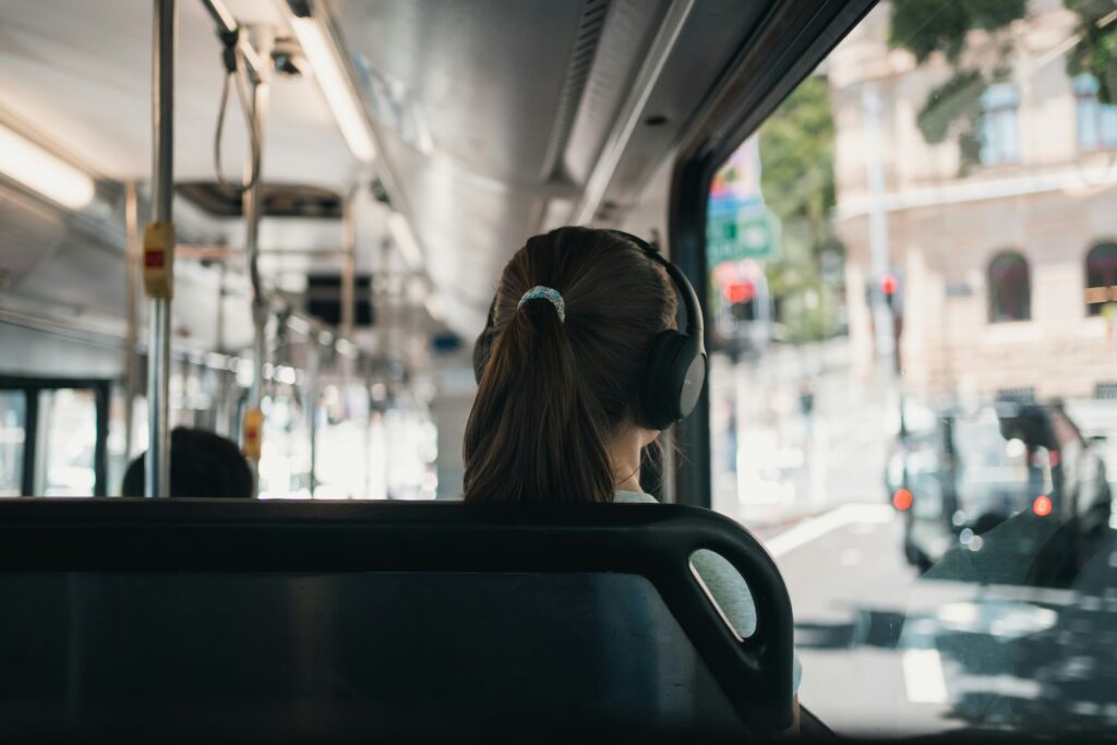 A girl wearing headphones traveling on a bus.