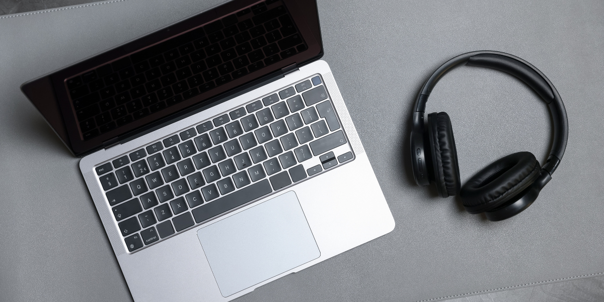 A photo of a silver laptop and black headphones on a grey desk.