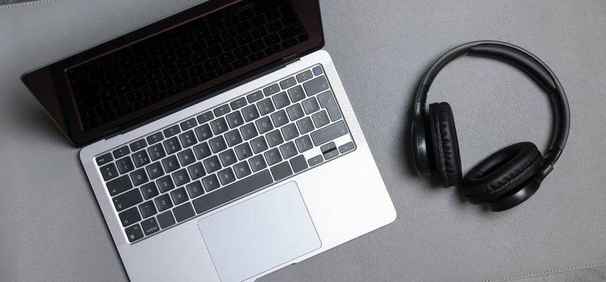 A photo of a silver laptop and black headphones on a grey desk.