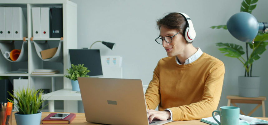 Young man with dark hair and glasses sitting in front of a laptop, and wearing headphones.