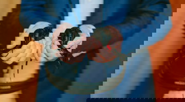 A man wearing a dark blue business suit and pale blue shirt, holding black headphones our in front of him.